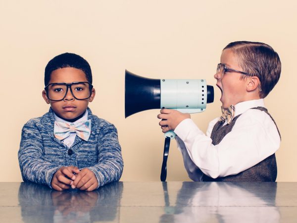 A young boy nerd shouts at the top of his voice to his co-worker through a megaphone trying to talk some sense into him but he is not listening and is ignoring him. The young nerds are dressed in bowties and glasses. Retro styling.