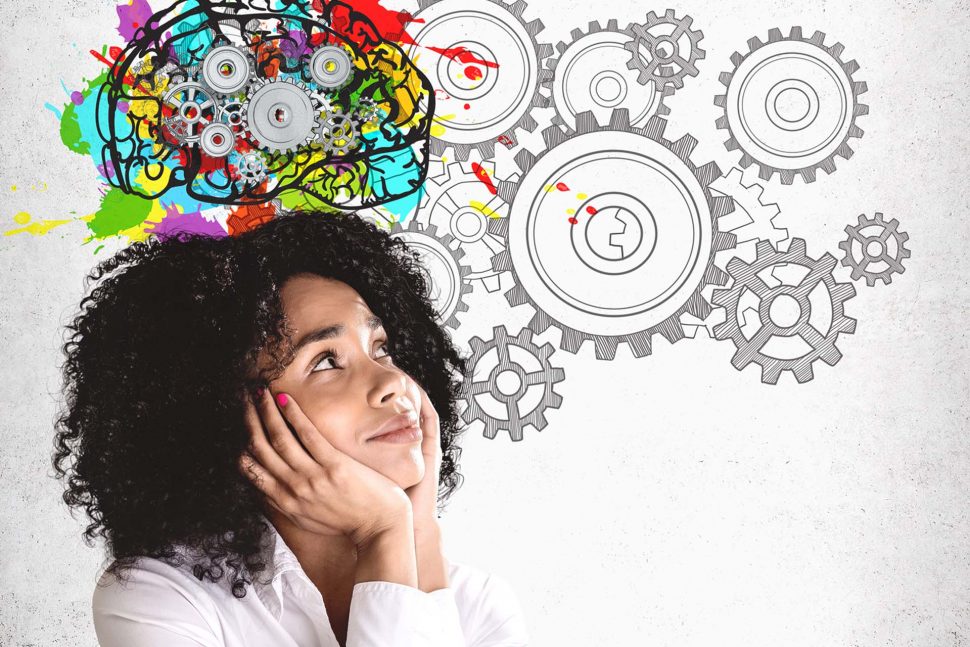 Girl thinking about cognitive dissonance Smiling young African American woman in white shirt looking at colorful brain sketch with gears drawn on concrete wall. Concept of brainstorming