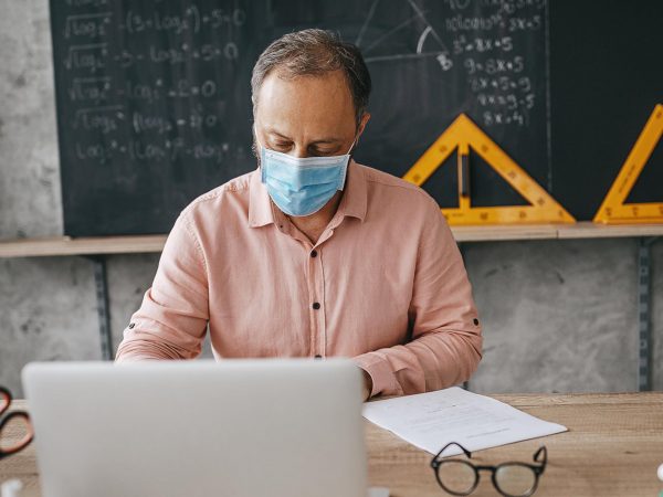 High school professor in classroom using laptop and wearing n95 face mask